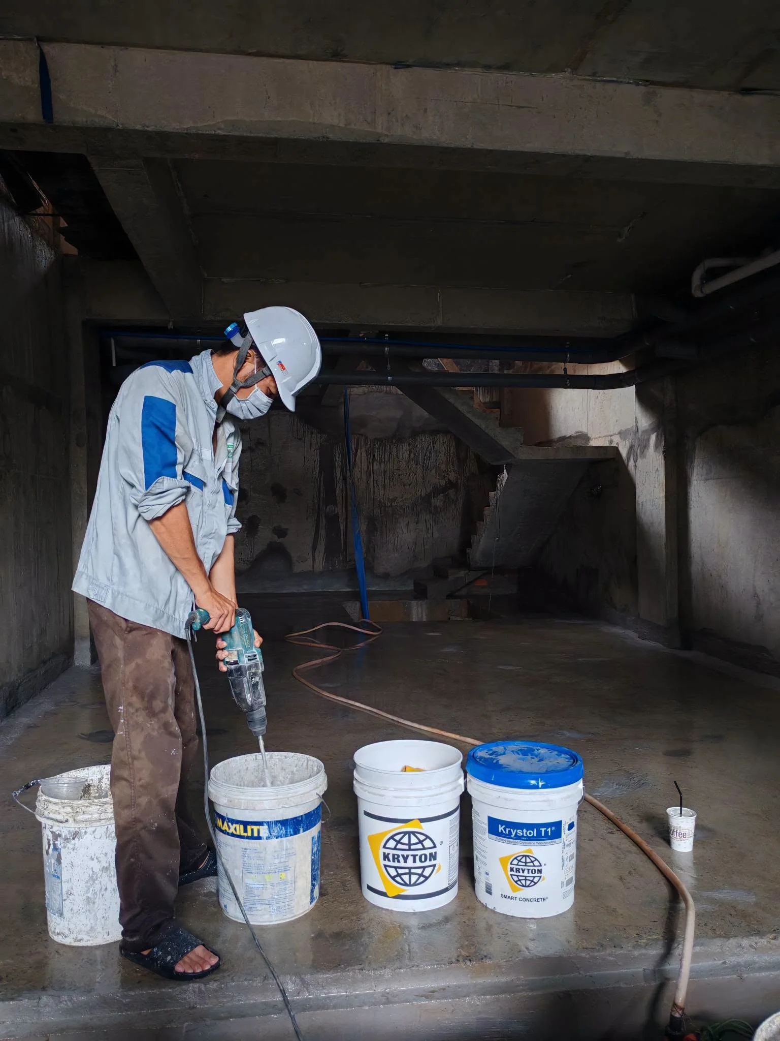 Thợ xây trộn vật liệu chống thấm bằng máy khoan tại tầng hầm