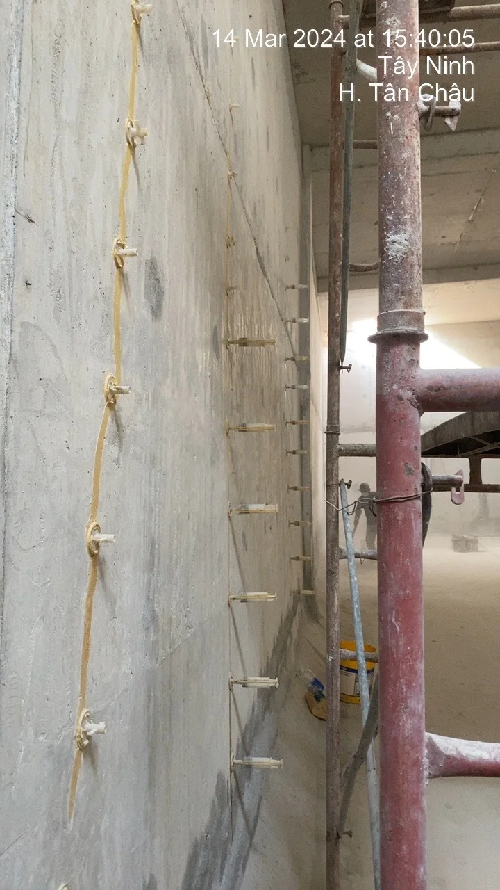 Tường bê tông được xử lý chống thấm bằng mũi kim tiêm chuyên dụng, giàn giáo và ống kim loại trong công trình xây dựng.